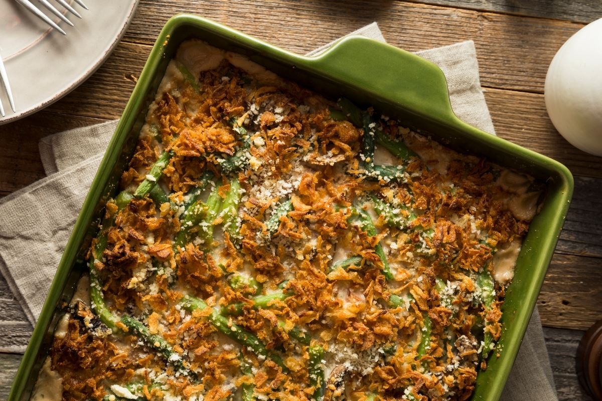 Photo of green bean casserole in a green baking dish on a rustic table setting.